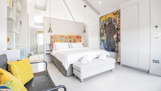 A modern hotel room with a bed, a sofa, a large wardrobe, and a colorful abstract painting on the wall. - The Grand Camden Garden 5BR Home (London)