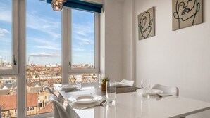 A dining area with a table set for two, large windows with a city view, and abstract wall art. - Modern Charming 2 bed Flat With Amazing Views (London)