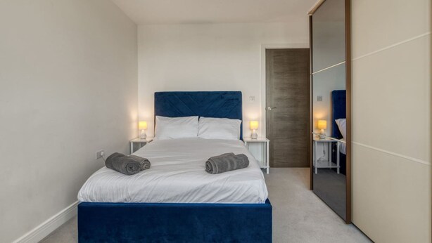 A bedroom with a bed, bedside tables, a mirror, and a wardrobe. - Modern Charming 2 bed Flat With Amazing Views (London)