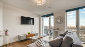 A modern living room with a flat-screen TV, a sofa, a coffee table, and a balcony with a view. - Modern Charming 2 bed Flat With Amazing Views (London)