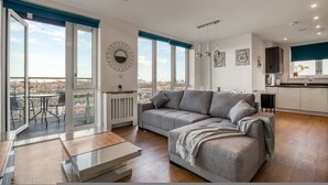 A modern apartment with a grey sofa, a dining table, and a kitchen area. - Modern Charming 2 bed Flat With Amazing Views (London)