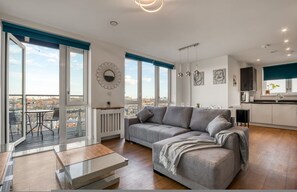 A modern apartment with a grey sofa, a dining table, and a kitchen area. - Modern Charming 2 bed Flat With Amazing Views (London)