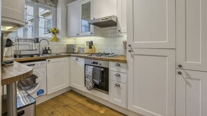 A kitchen with white cabinets, a built-in oven, a dishwasher, and a window with a view of the outside. - Comfortable 2-bed in Zone 2 (London)