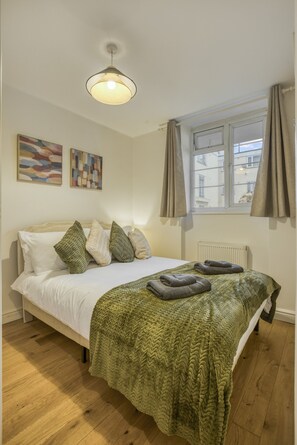 A bedroom with a bed, a window with curtains, a radiator, and artwork on the wall. - Comfortable 2-bed in Zone 2 (London)