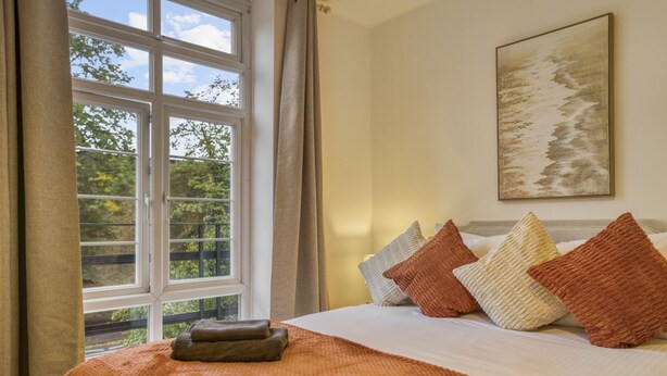 A hotel room with a large window, a bed with multiple pillows, and a painting on the wall. - Comfortable 2-bed in Zone 2 (London)