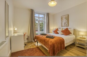 A bedroom with a bed, a nightstand, a window, and a radiator. - Comfortable 2-bed in Zone 2 (London)