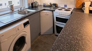 Una cocina compacta con lavadora, lavavajillas, estufa y una ventana con vista a un edificio.