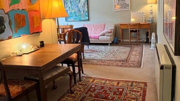 Una sala de estar con una mesa de comedor, dos sofás, un tapete y un cuadro en la pared.