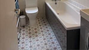 Un baño con inodoro, bañera, ventana y vista a un edificio.