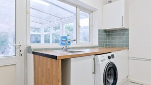 A compact kitchen with a washing machine, a sink, and a window with frosted glass. - Group-Friendly Home | TV in Every Room, WiFi & Parking (Bon-y-maen)