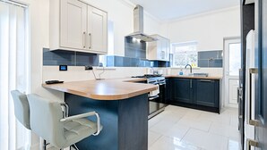 A modern kitchen with a central island, built-in oven, and stainless steel appliances. - Group-Friendly Home | TV in Every Room, WiFi & Parking (Bon-y-maen)