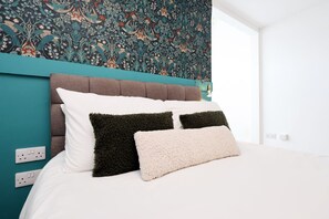 Un letto con biancheria bianca, una parete color petrolio e carta da parati decorata.