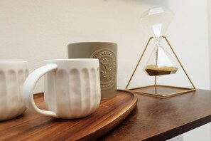 Una bandeja de madera con dos tazas blancas y una taza marrón con un logotipo, y una ampulleta dorada sobre una mesa.