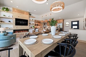 A modern kitchen with a wooden dining table set for six, a fireplace, and a TV mounted on the wall. - Beach•Arcade•Hot tub•Putting Green•Dog-friendly! (New Lisbon)