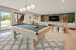 Un salon moderne équipé d’une table de billard, d’un téléviseur et d’un escalier menant à un espace extérieur.