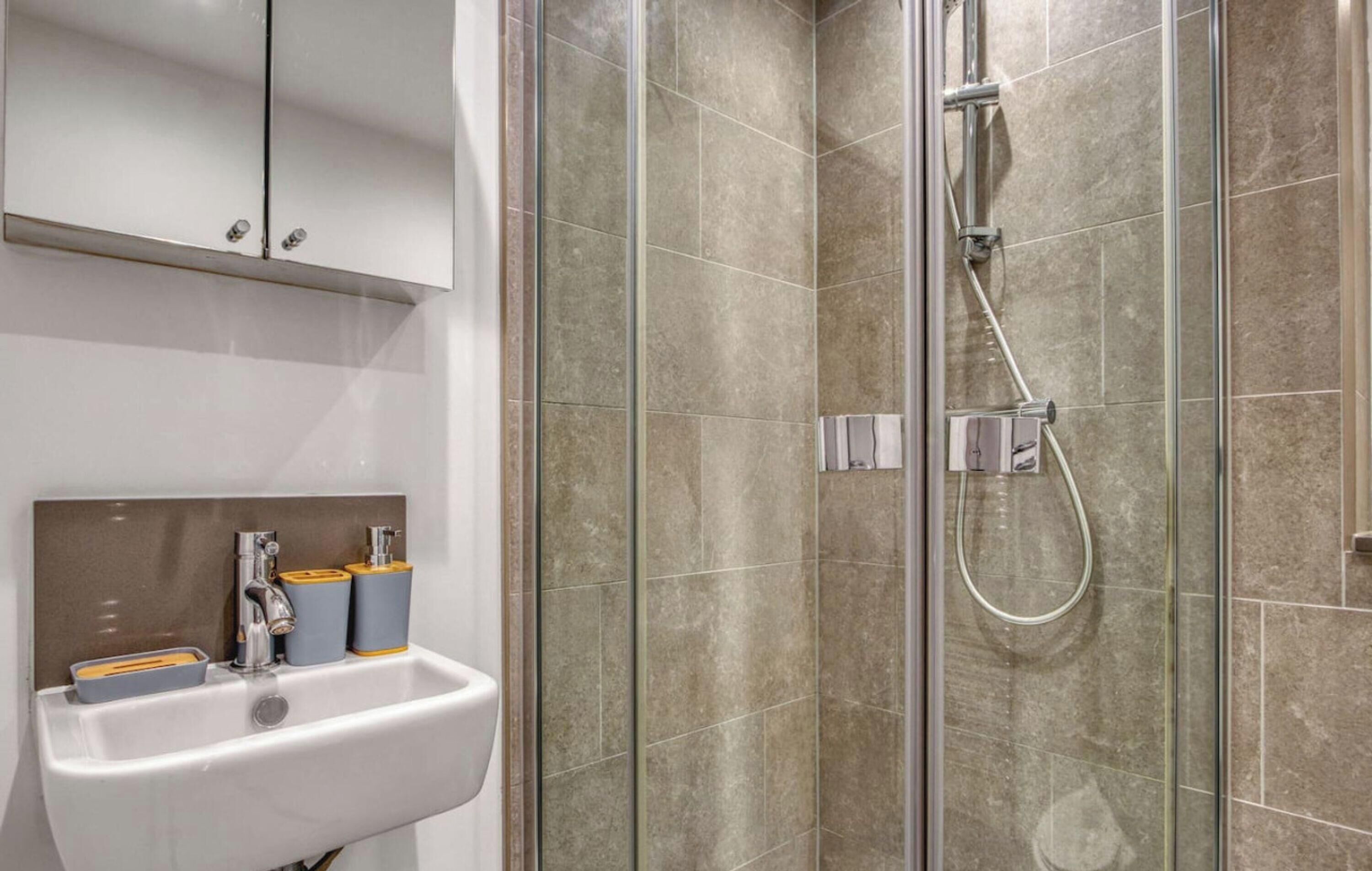 A modern bathroom with a glass-enclosed shower, a white sink, and a mirror above it.