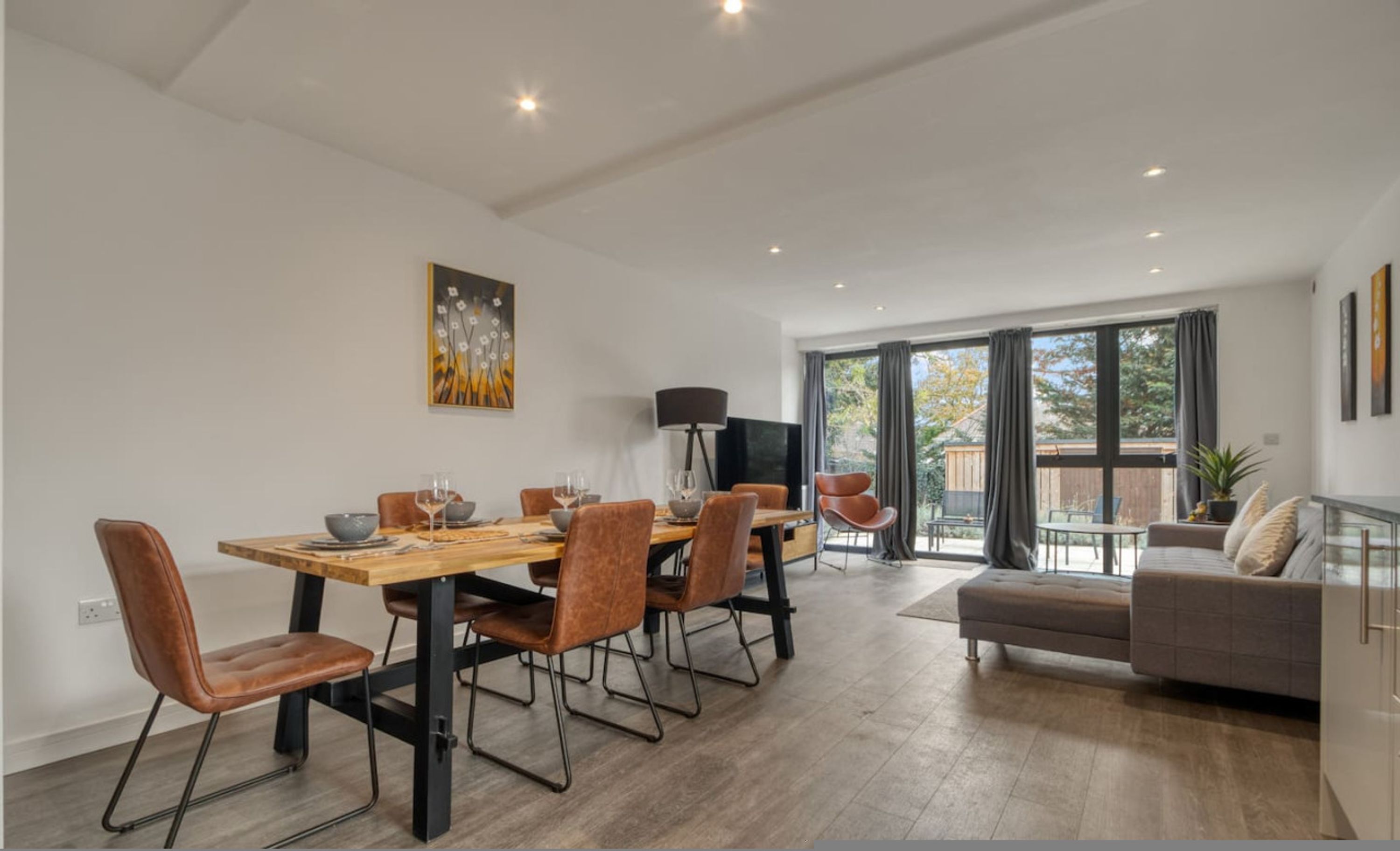 Ein moderner Essbereich mit Holztisch und Stühlen, einem Fernseher und einem Balkon mit einer Sitzecke.
