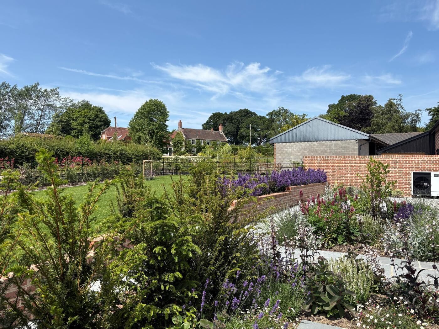 A garden with various plants and a building with a brick wall and a metal roof.