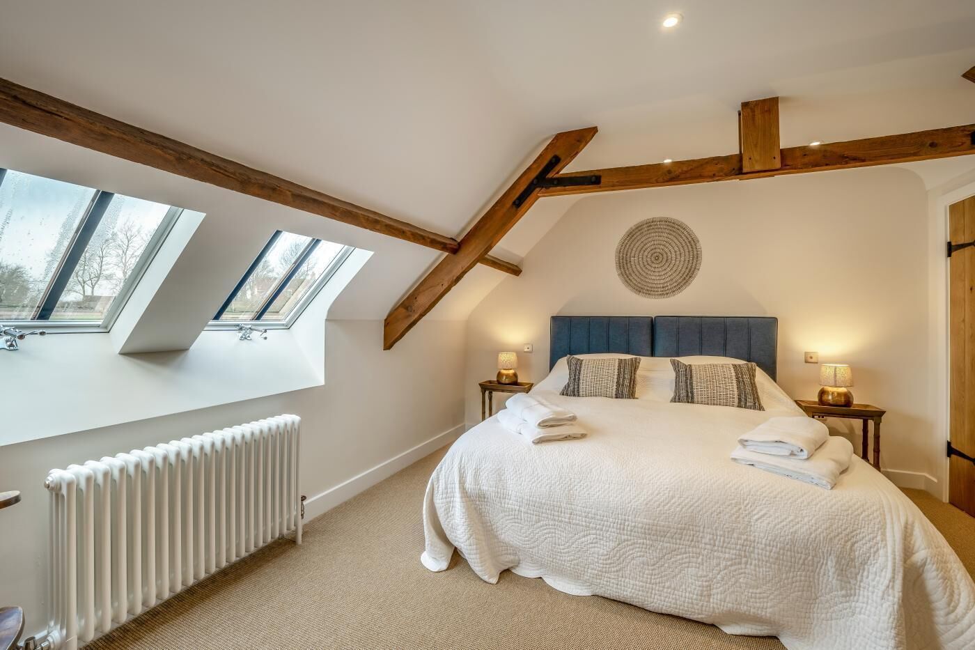 A bedroom with a large bed, skylights, a radiator, and a round wall decoration.