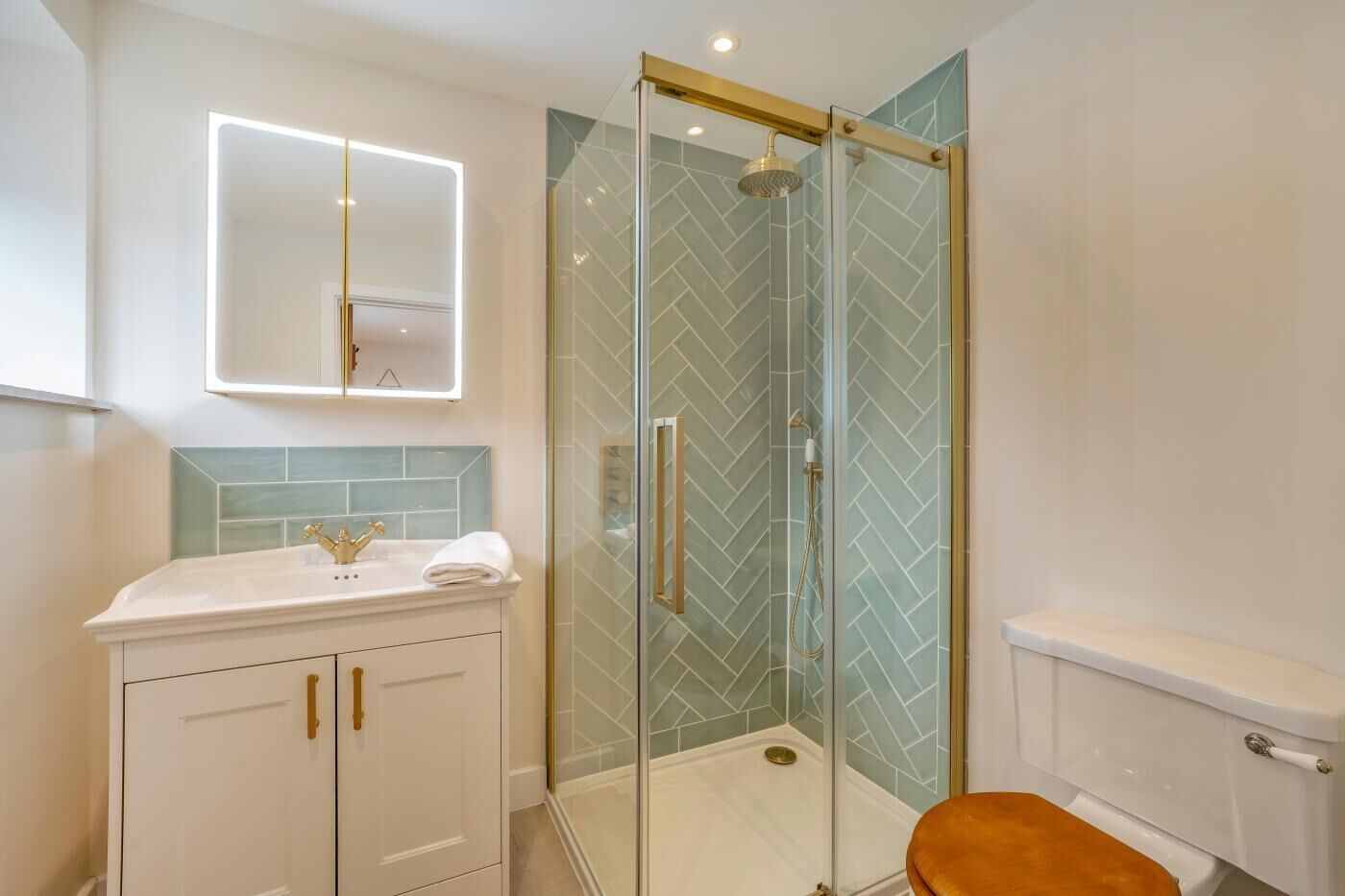 A modern bathroom with a glass-enclosed shower, a white vanity with gold handles, and a toilet.