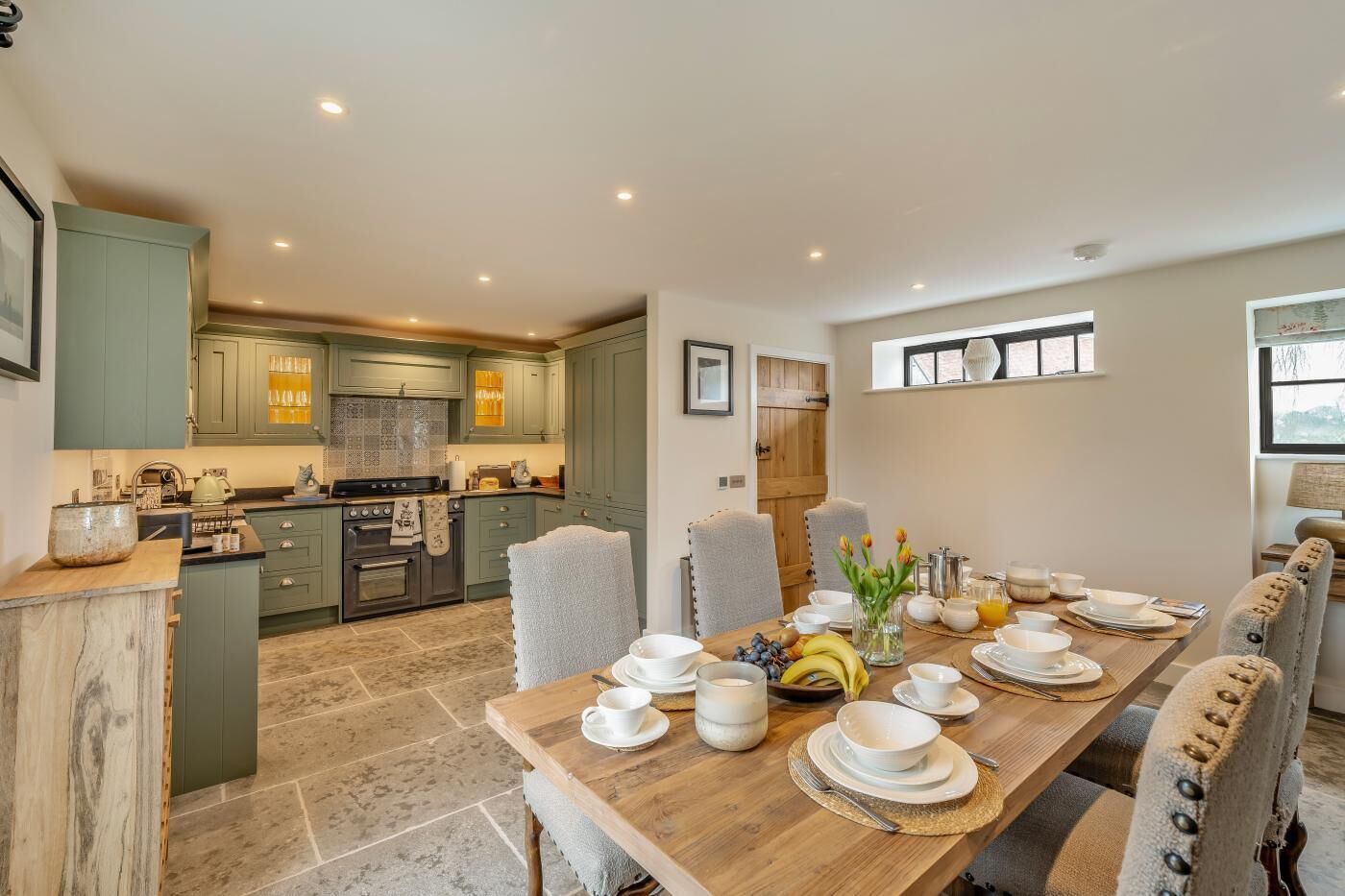 A spacious kitchen with green cabinets, a dining area with a wooden table set for four, and a view of the adjacent dining room.