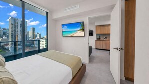 A modern hotel room with a large bed, a TV, a city view, and a kitchenette. - Skyline View 1BR + Den Near Port Miami (Miami)