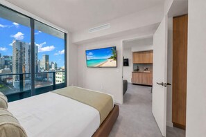 Ein modernes Hotelzimmer mit einem großen Bett, einem Fernseher, Blick auf die Stadt und einer Küchenzeile.