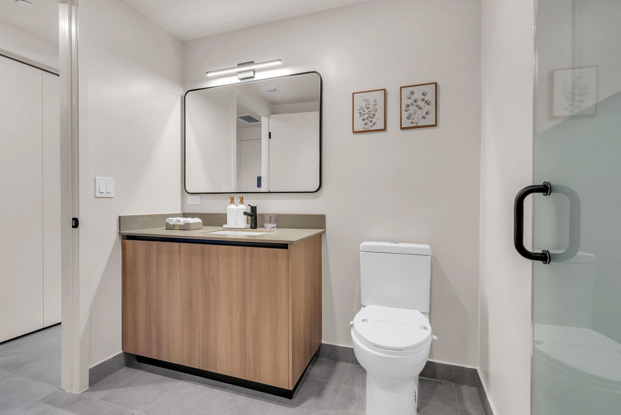 A modern bathroom with a wooden vanity, a white toilet, and a large mirror.