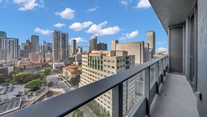 A cityscape view from a balcony with modern buildings, a clear sky, and a street below. - Skyline View 1BR + Den Near Port Miami (Miami)