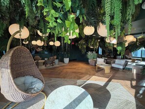 Ein Zimmer mit hängenden Pflanzen, Korbstühlen und runden Tischen.