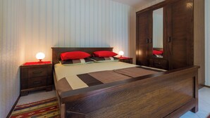 A bedroom with a wooden bed, red pillows, a nightstand with a lamp, and a wardrobe. - Apartment created for enjoyment (Crikvenica)