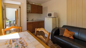 A compact living space with a dining table, a sofa, a kitchen area including a refrigerator and microwave, and a patterned rug. - Apartment created for enjoyment (Crikvenica)