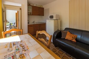 A compact living space with a dining table, a sofa, a kitchen area including a refrigerator and microwave, and a patterned rug. - Apartment created for enjoyment (Crikvenica)
