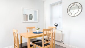 A dining area with a wooden table and chairs, a potted plant, a mirror, and a wall clock. - Spacious 3BR Home Sleeps 7 | Parking, WiFi & Near Centre (Plasmarl)