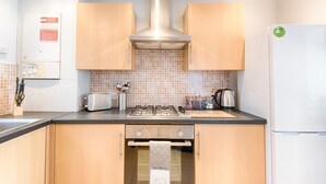 A kitchen with wooden cabinets, a gas stove, a toaster, and a refrigerator. - Spacious 3BR Home Sleeps 7 | Parking, WiFi & Near Centre (Plasmarl)