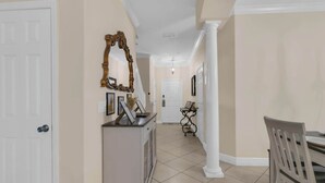 A hallway with a white door, a console table with framed pictures, a dining area with a table and chairs, and a mirror on the wall. - Mouse House 5 miles to Disney sleeps 9 (Kissimmee)