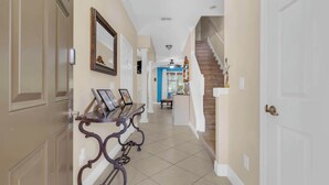 A hallway with a console table displaying framed pictures, a staircase with a wooden handrail, and a ceiling fan. - Mouse House 5 miles to Disney sleeps 9 (Kissimmee)