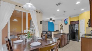 A modern kitchen with a dining area, a ceiling fan, and a TV mounted on the wall. - Mouse House 5 miles to Disney sleeps 9 (Kissimmee)