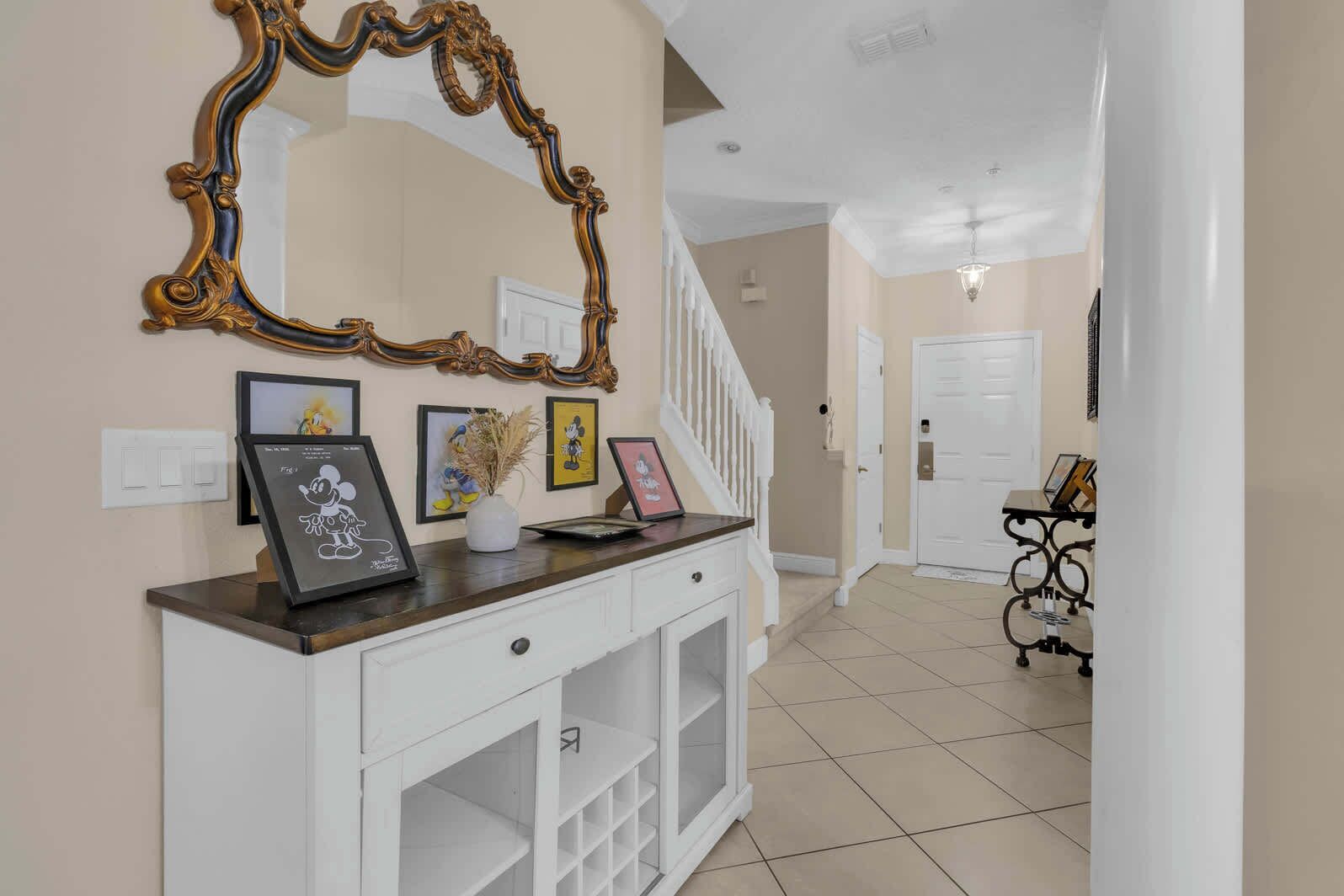 A hallway with a white console table, framed pictures, a decorative mirror, and a staircase.