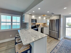 A modern kitchen with a marble countertop, stainless steel appliances, and a large island with seating. - Pointe South 407 | Unwind by the Gulf, Stunning Views + Pool (Fort Myers Beach)