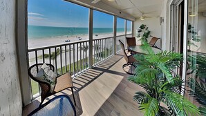 Een balkon met uitzicht op het strand, rieten stoelen, een tafel en planten in potten.