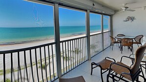 Un balcon avec vue sur la plage, des meubles en osier et un ventilateur de plafond.