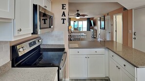A kitchen with white cabinets, a black stove, and a ceiling fan. - Pointe South 503 | Gulf Views + Heated Pool (Fort Myers Beach)