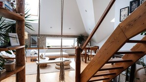 Un habitación estilo loft con escalera de madera, una silla colgante y vistas al área de estar.