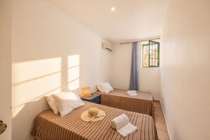 Ein Zimmer mit zwei Betten, einem Nachttisch, einer Lampe und einem Fenster mit Vorhang.