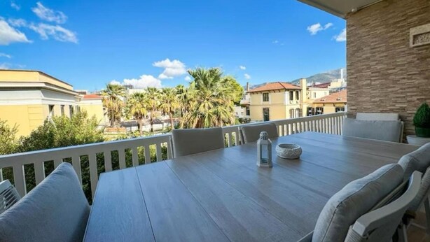 Een balkon met een tafel en stoelen, uitkijkend op een woonwijk met palmbomen en gebouwen.