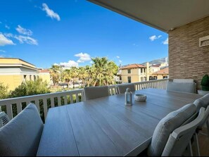 A balcony with a table and chairs, overlooking a residential area with palm trees and buildings. - Elegant VIP Apartment - Athens Town (Athina)