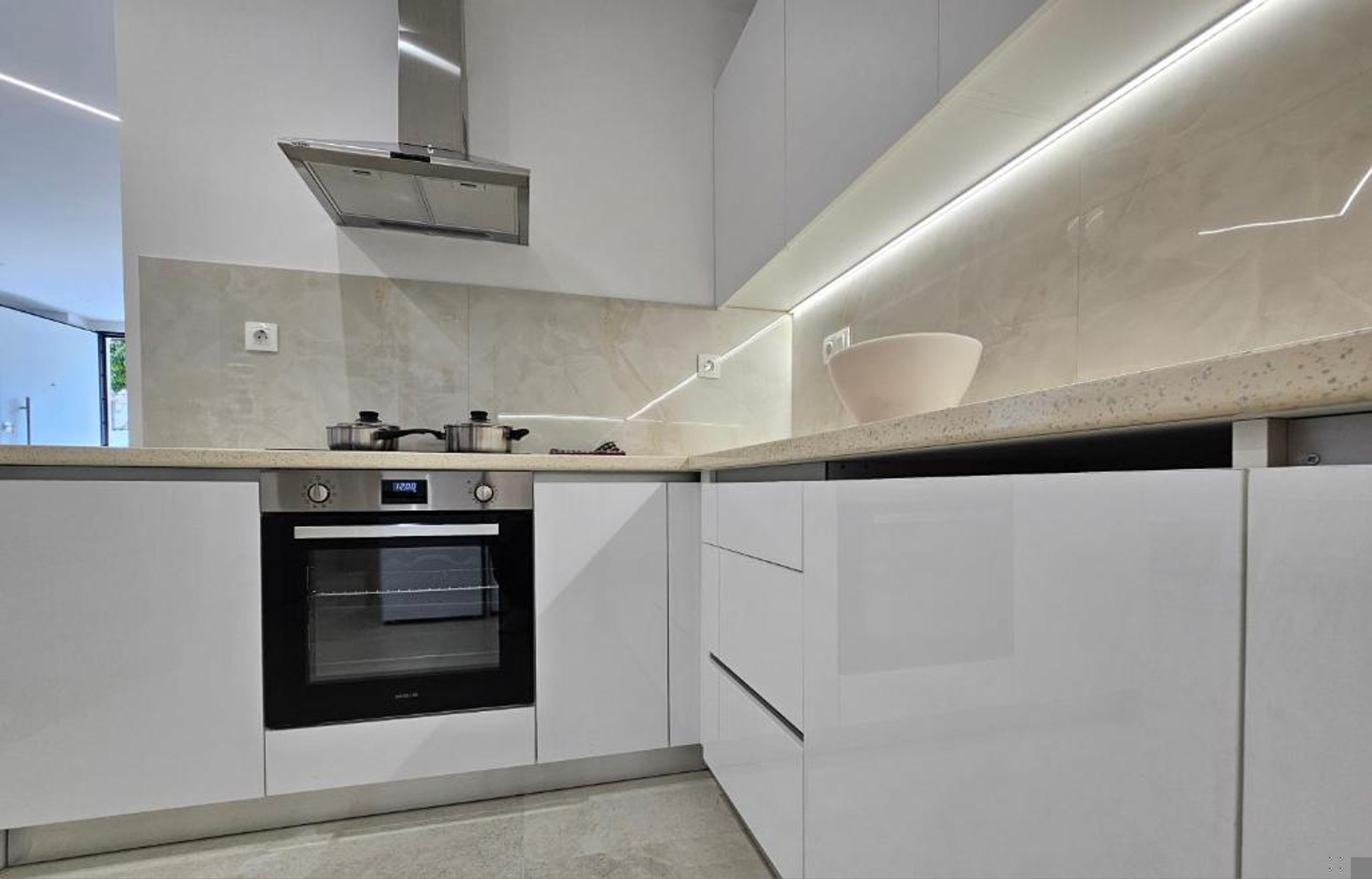 Een moderne keuken met een ingebouwde oven, een roestvrijstalen afzuigkap en een aanrecht met een kom.