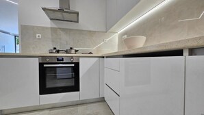 A modern kitchen with a built-in oven, a stainless steel range hood, and a countertop with a bowl. - Sagar Residential Apartment - Athens Town (Nea Ionia)