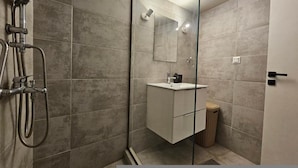 Un baño moderno con cabina de ducha de vidrio, tocador blanco y un cubo de basura.